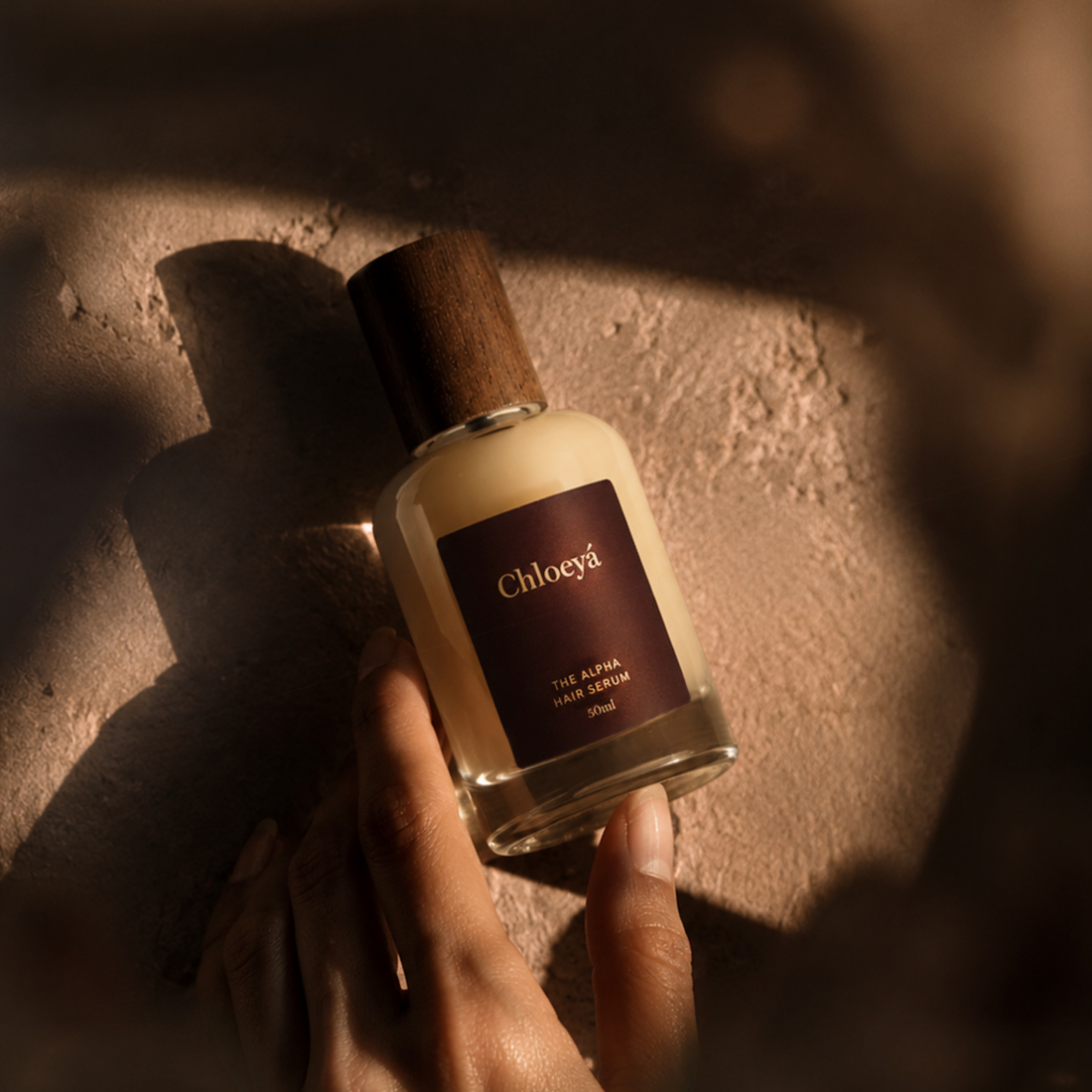 A hand holding the Alpha Hair Serum bottle up to the light, the level of serum left in it visible against the label