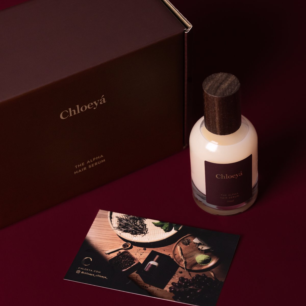 The Alpha Hair Serum bottle standing beside its box and a printed card on a deep crimson surface